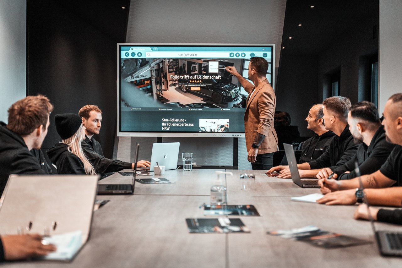 Das StarFolierung Team in einer Besprechung vor dem großen Screen